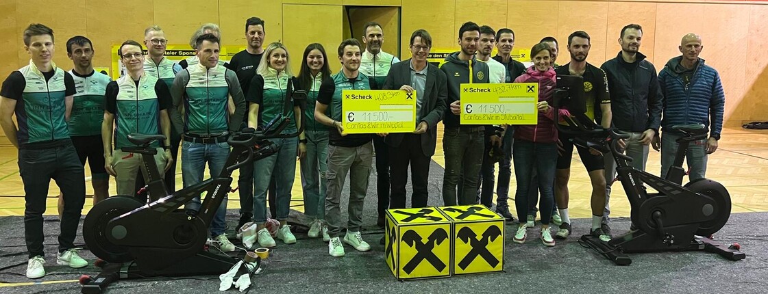 Gruppenfoto in einer Sporthalle. Zwei Perosnen präsentieren jeweils einen Spendenscheck über 11.500 Euro.