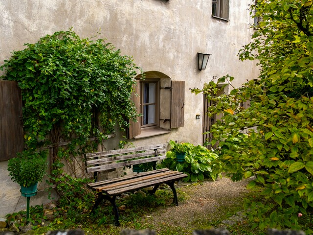 Eine alte Holzbank steht im Garten an der Hauswand eines alten, malerischen Hauses.
