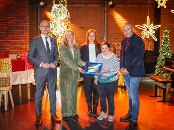 Fünf Personen stehen in einem weihnachtlich dekorierten Raum zu einem Gruppenfoto zusammen und präsentieren einen Spendenscheck über 6.000 Euro..