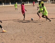 Fußball unterstützt Straßenkinder, traumatische Erfahrungen zu verarbeiten und Teamgeist zu entwickeln. © Caritas Zwei Spieler kämpfen während eines Fußballspiels auf Sandboden um den Ball.