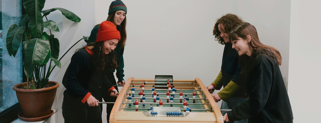 Vier junge, lachende Frauen spielen gemeinsam Tischfussball.