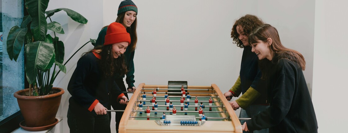 Vier junge, lachende Frauen spielen gemeinsam Tischfussball.