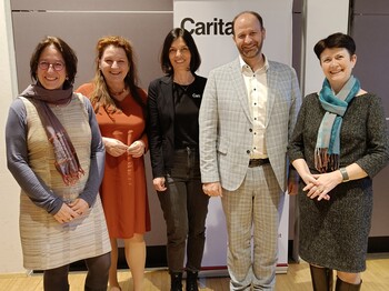Fünf Personen stehen vor einem Caritas Roll-Up zu einem Gruppenfoto zusammen.
