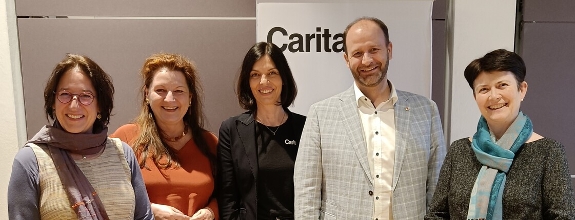 Fünf Personen stehen vor einem Caritas Roll-Up zu einem Gruppenfoto zusammen.