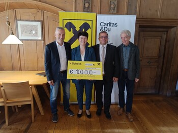 Vier Personen stehen vor einem Roll-Up der Raiffeisenbank und einem der Caritas.