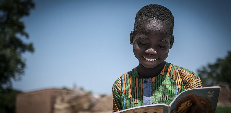 Ein afrikanischer Junge in buntem T-Shirt liest in einem Comic Heft.