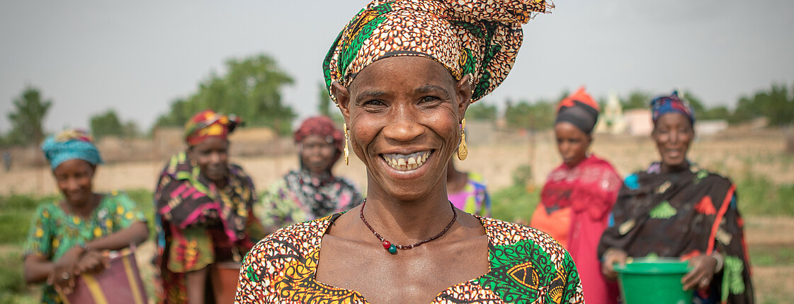 Eine Frau mit buntem Kleid und Kopftuch steht vor einem Bewässerungsbrunnen in der Region Kayes in Mali.