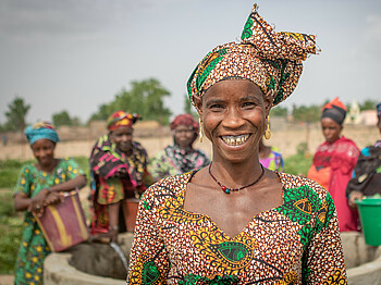 Eine Frau mit buntem Kleid und Kopftuch steht vor einem Bewässerungsbrunnen in der Region Kayes in Mali.
