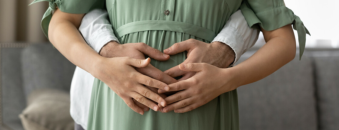 Eine Schwangere und der werdende Vater legen ihre Hände gemeinsam auf dem Babybauch ab.