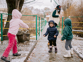 Drei Kinder spielen mit ihrer Betreuerin im Regen