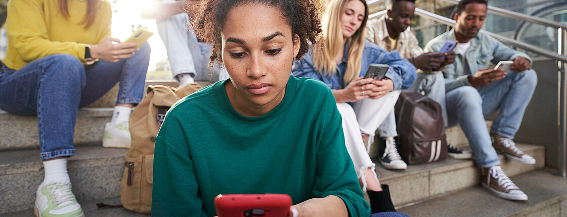 Sechs Jugendliche sitzen auf einer Betontreppe und schauen in ihre Smartphones.