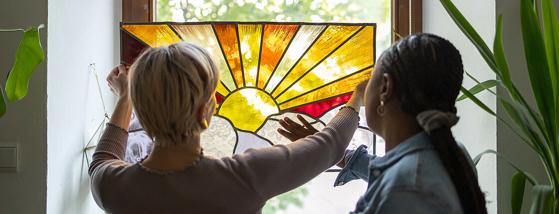 Zwei Frauen begutachten eine künstlerisch bemalte Glasscheibe.