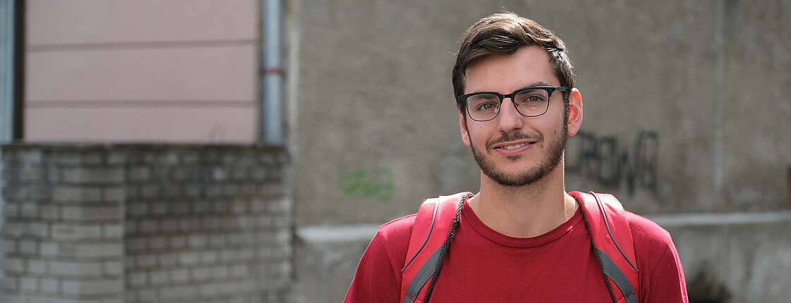 Portrait eines jungen Mannes mit Brille und rotem Caritas T-Shirt und Rucksack. 