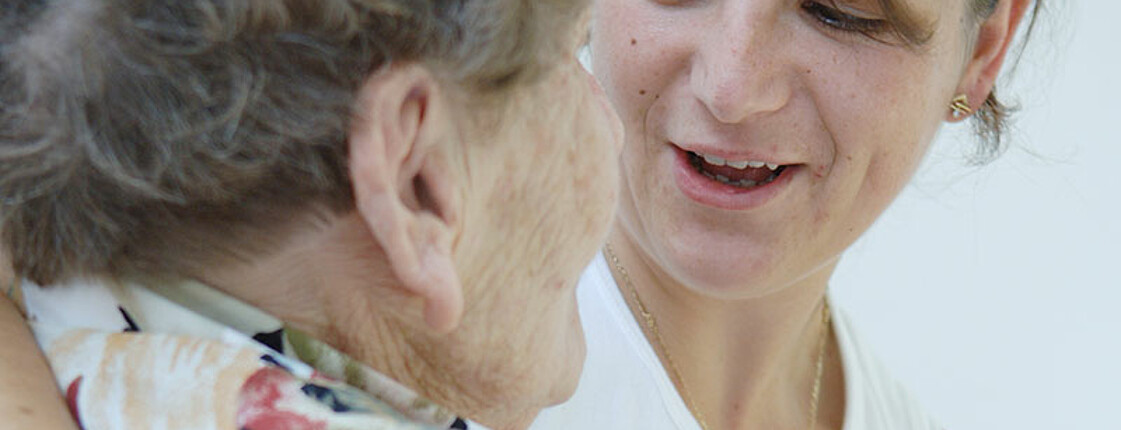 Eine Betreuerin umarmt eine alte Dame, die an Demenz erkrankt ist.