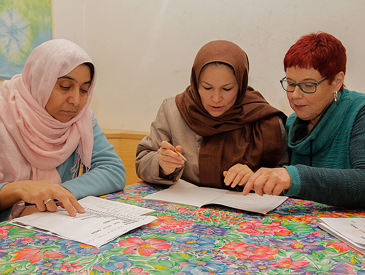 Eine Frau unterstützt zwei Frauen mit Kopftuch beim Lernen