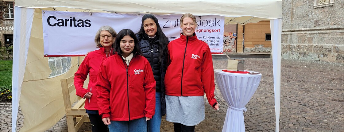 Vier Frauen mit roten Caritas Jacken stehen vor einem Pavillon.