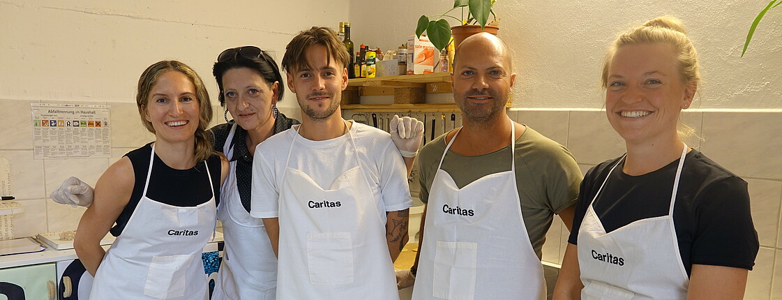 Fünf Personen mit weißen Caritas-Küchenschürzen stehen zu einem Gruppenfoto zusammen.