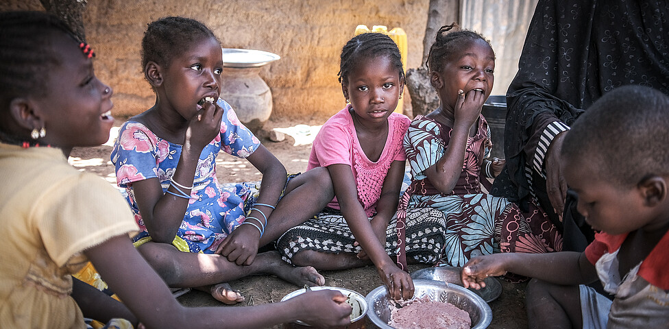 Fünf Kinder sitzen im Kreis um zwei Schüsseln und essen mit den Händen.