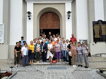 Viele Personen stehen vor einer Kirche zu einem Gruppenfoto zusammen.