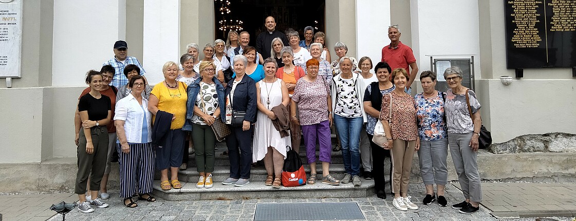 Viele Personen stehen vor einer Kirche zu einem Gruppenfoto zusammen.