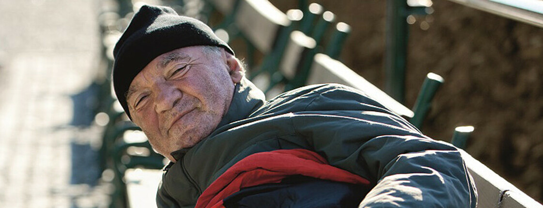 Ein Mann mit Wintermütze und Schlafsack liegt auf einer Parkbank.