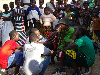 Eine große Gruppe Kinder steht im Kreis um ein paar Jugendliche, die musizieren.