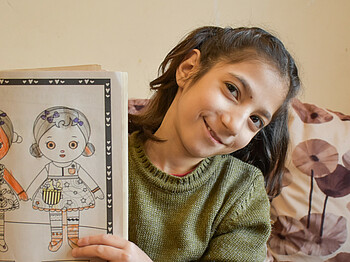 Ein Mädchen hält ein Heft mit selbstgemalten Bildern hoch.