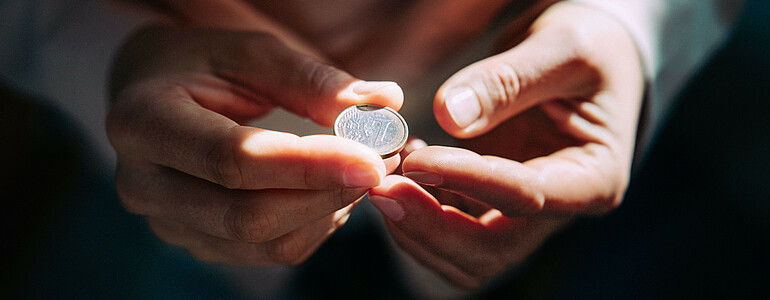 Zwei Hände halten eine Ein-Euro-Münze.