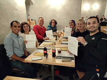 Gruppenfoto von sieben Personen in einem Restaurant. Alle Personen halten Urkunden hoch.