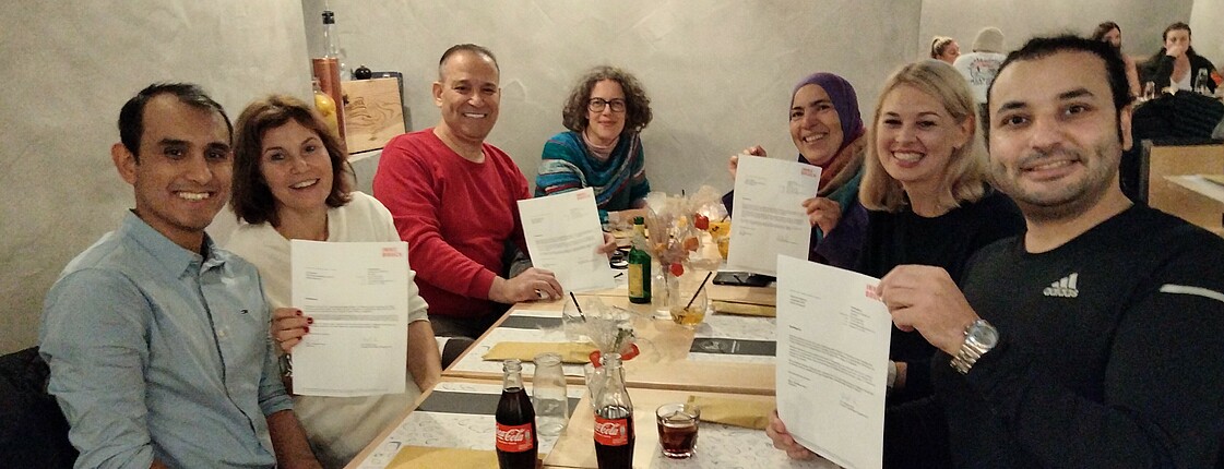 Gruppenfoto von sieben Personen in einem Restaurant. Alle Personen halten Urkunden hoch.