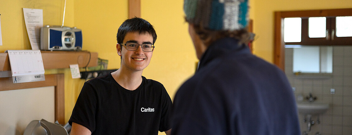 In einer Wärmestube ist ein Caritas-Mitarbeiter im Gespräch mit einem Klienten.