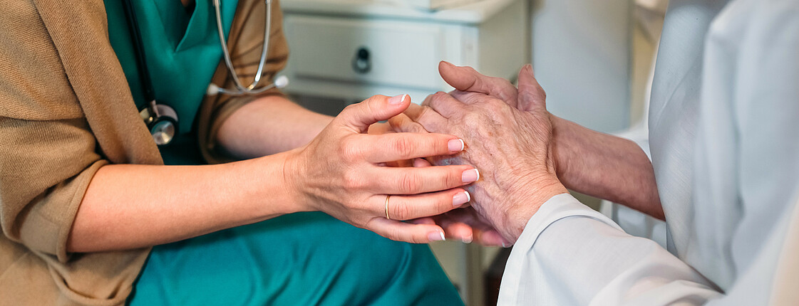 Eine Krankenschwester hält die Hände einer Seniorin.