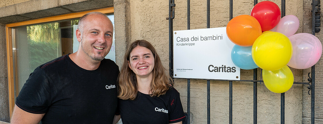 Ein Mann und eine Frau stehen neben eine Plakette mit der Aufschrift „Casa die bambini. Kinderkrippe“.