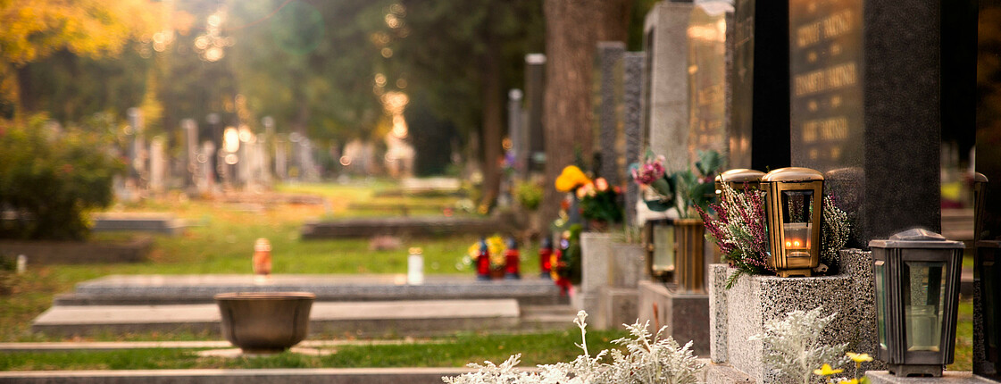 Eine Reihe Gräber mit Grabblumen auf einem Friedhof im Herbst.